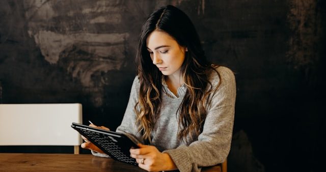 Eine Frau sitzt an einem Tisch und blickt auf einen Tablet-PC.